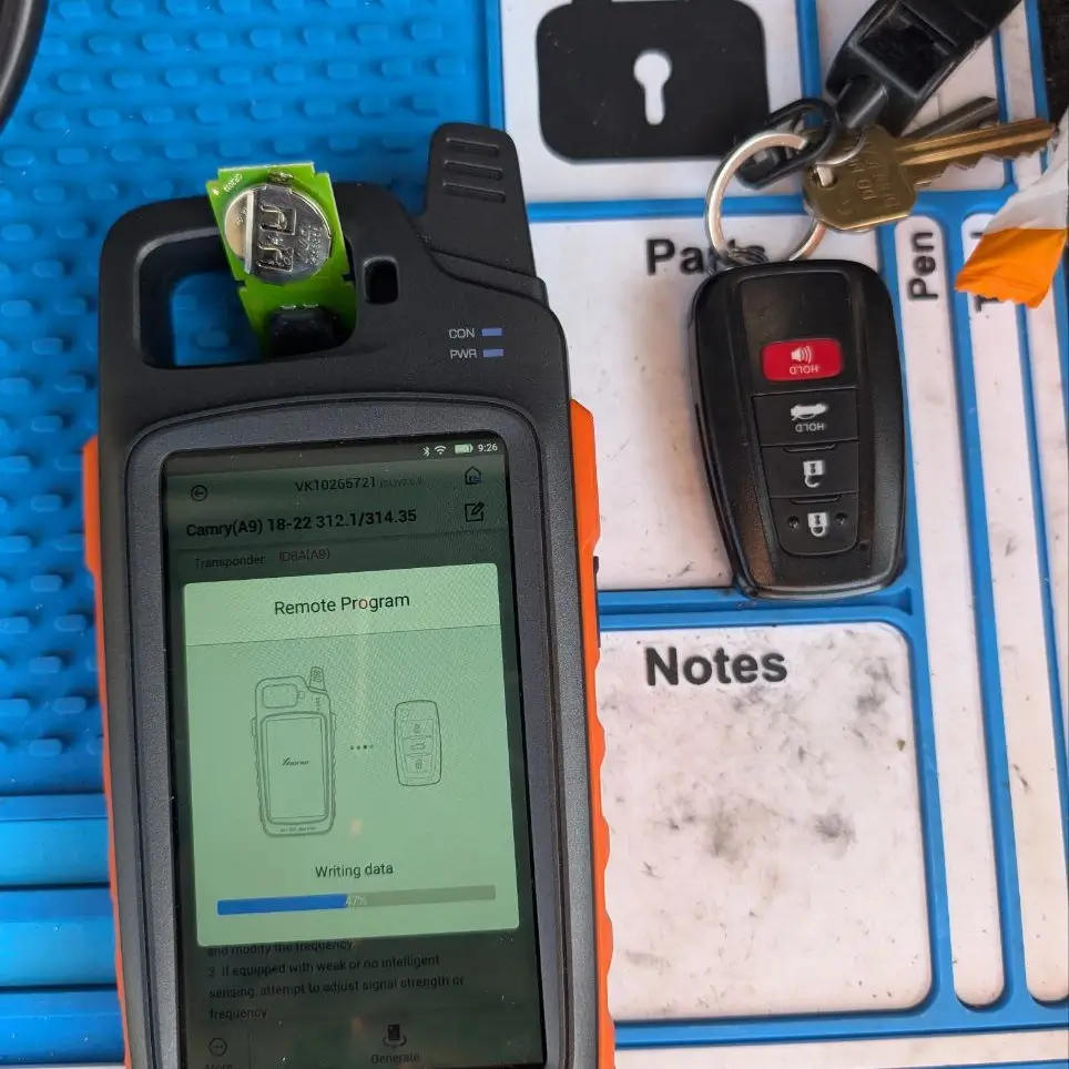 A technician's hands programming a car key fob using a special device.