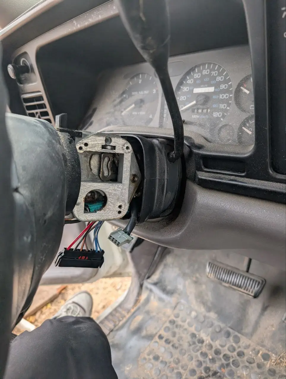 Exposed steering column with disconnected ignition switch wiring in a vehicle interior.