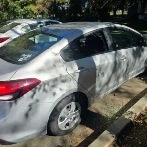 Exterior of silver Kia Forte with broken driver-side window during ignition repair project